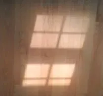 Soft sunlight casts a grid-like window shadow on a textured wooden floor, creating a warm and serene atmosphere.