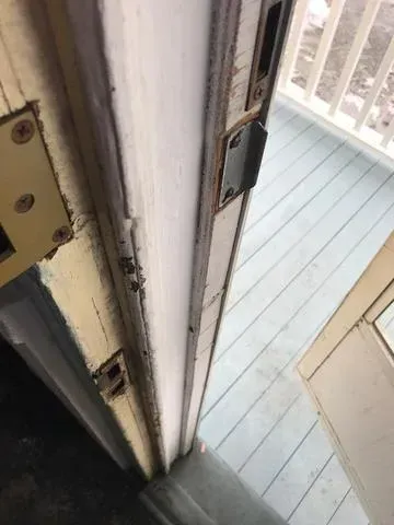 A close-up of a white door frame shows visible wear and rusted metal parts. The door is ajar, revealing a wooden deck outside with pale blue flooring.