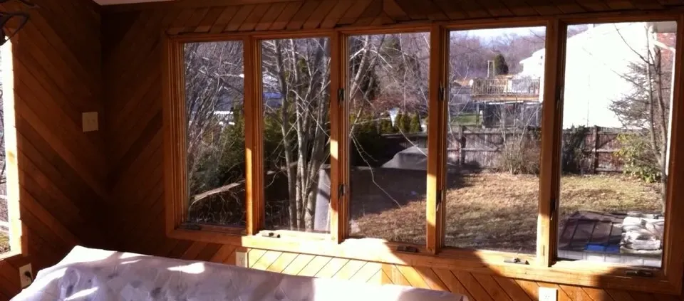 A cozy sunroom with wooden paneled walls and large windows showing a sunlit backyard. The scene is warm and inviting, with natural light filling the space.