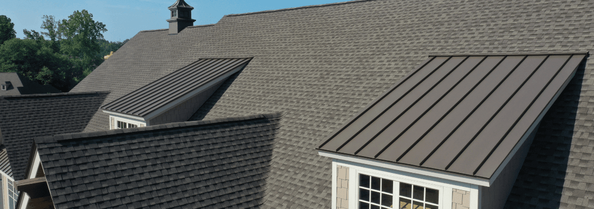 A gabled roof with dark brown shingles and window dormers, each with a metal roof. Trees in the background create a serene and rural atmosphere.