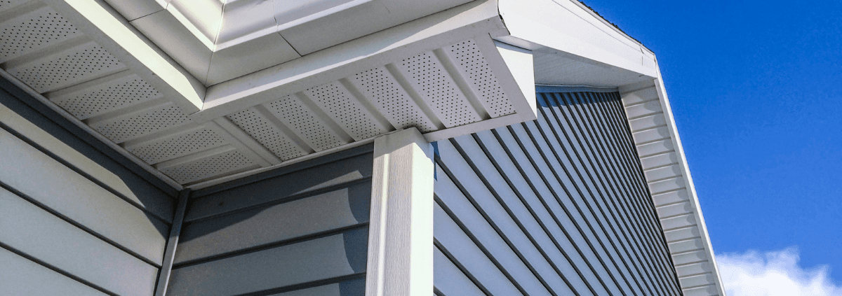 Close-up of house siding with neatly aligned horizontal panels under a clear blue sky. The white soffit and eaves create a clean, modern look.