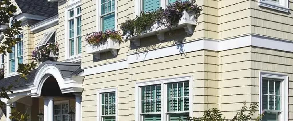 A charming house exterior with cream siding and teal shutters. Flower boxes with vibrant blooms adorn the windows, adding a welcoming touch.