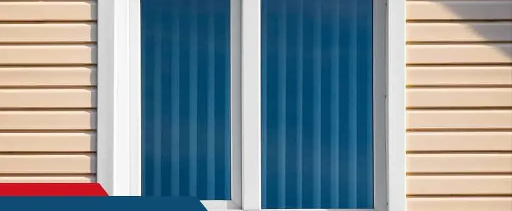 A window with white trim set in beige siding, featuring two blue vertical striped curtains. The scene is simple and conveys a feeling of calm and order.