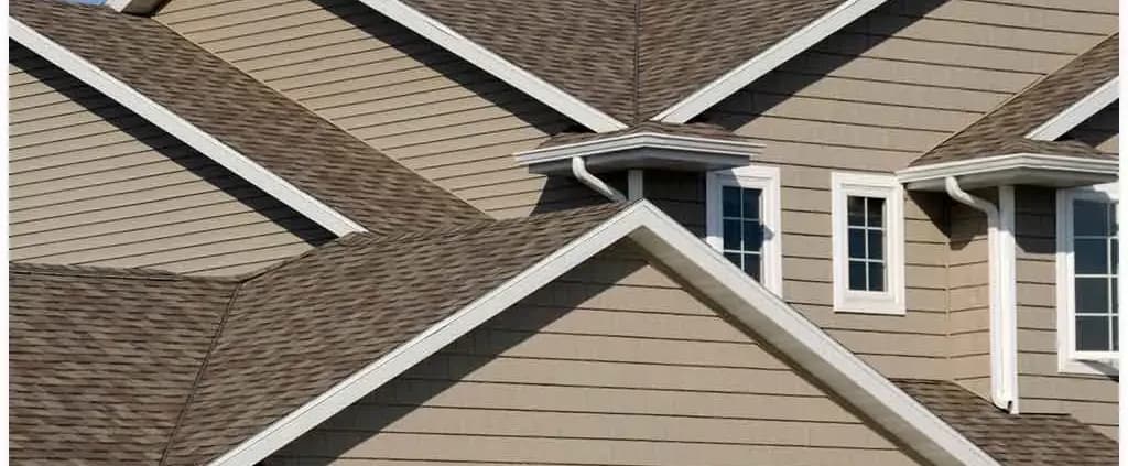 A cluster of gabled roofs with brown shingles and beige siding, featuring white trim and several windows. The scene conveys a sense of neatness and order.