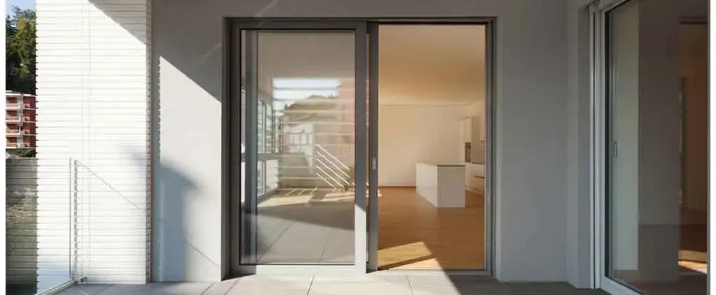 Modern patio with sliding glass doors leading to a sunlit, empty interior space with wooden floors and white walls. Minimalist and serene atmosphere.