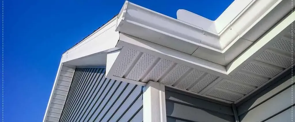 Close-up of a modern house exterior featuring gray vinyl siding and white soffit under a clear blue sky, conveying a sense of cleanliness and simplicity.