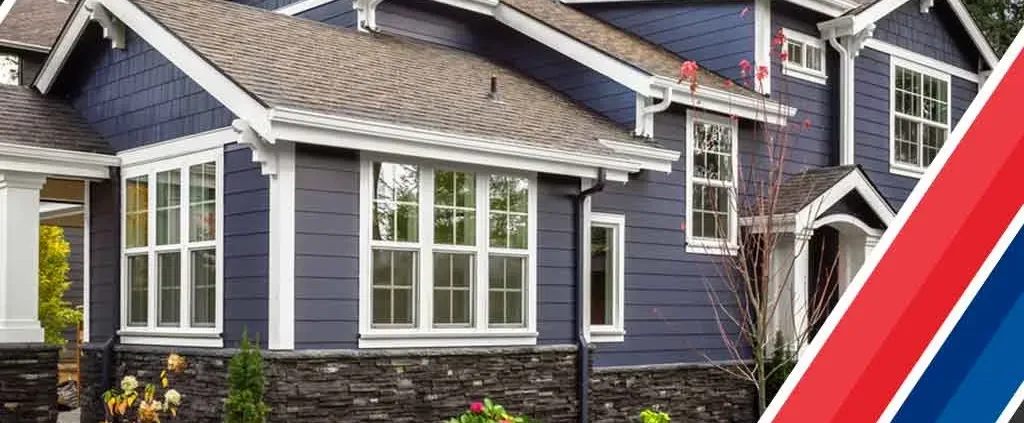 Modern two-story house with blue siding and white trim. Large windows, stone foundation, and a red, blue, and white corner accent.