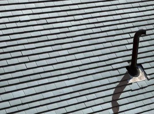 A slate roof with evenly spaced gray tiles features a dark vent pipe casting a shadow. The image conveys a sense of order and functionality.
