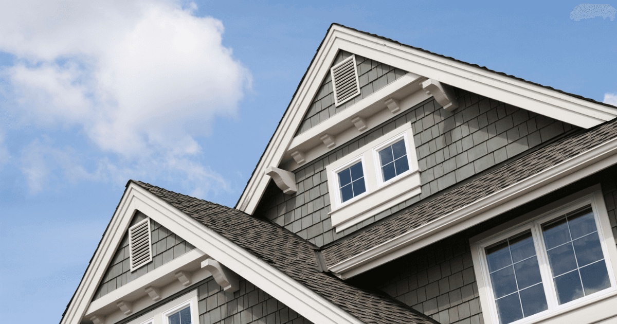 Gable roof house with gray shingles, white trim, and two upper windows. Clear blue sky with a few clouds, conveying a calm and welcoming atmosphere.