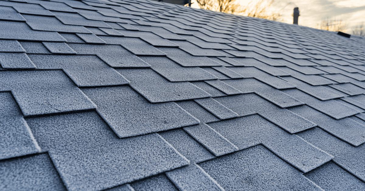 Close-up of a frost-covered shingle roof at sunrise, displaying geometric pattern of overlapping rectangles. The scene conveys a chilly, tranquil morning.