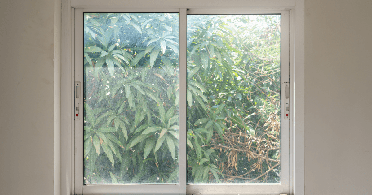 A sliding glass door partially open, revealing lush green leaves and vegetation outside. Natural light filters in, creating a calm, serene atmosphere.