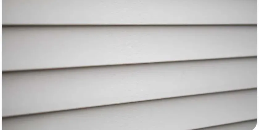 Close-up image of beige vinyl siding with horizontal panels, creating a sleek, uniform texture. The lighting suggests a neutral, calm atmosphere.