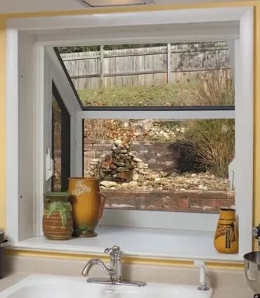 Kitchen window displaying a garden view with a stone wall. Three decorative vases sit on the windowsill, adding warmth to the bright interior.