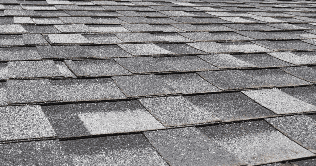 Close-up view of a roof with asphalt shingles in varying shades of gray, creating a textured and uniform pattern. The shingles appear orderly and well-maintained.