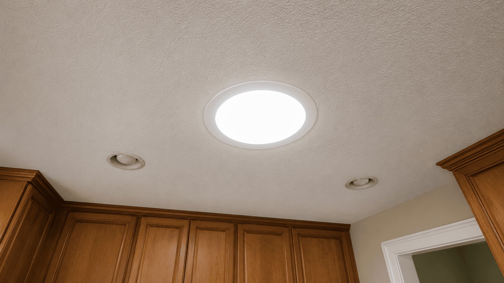Ceiling view with a bright circular light fixture centered, surrounded by textured surface and wooden cabinets below, creating a warm, inviting atmosphere.