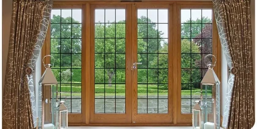 A large wooden-framed window with grid panes overlooking a lush garden. Elegant brown curtains and decorative lanterns flank the window, creating a serene, inviting ambiance.