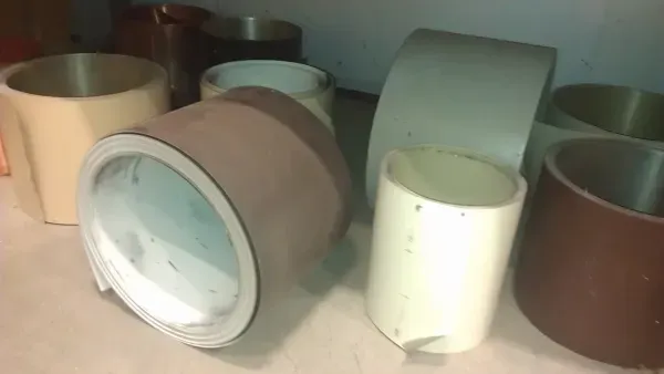 Large rolls of variously colored linoleum are stacked and scattered on a concrete floor. The rolls are brown, beige, and gray in a dimly lit space.