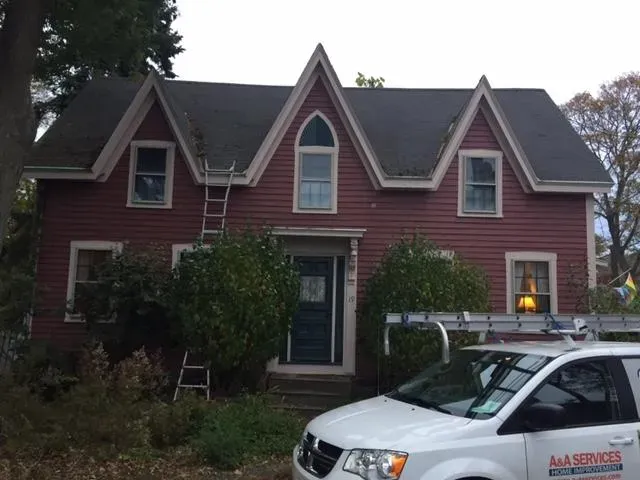 A charming two-story red house with pointed gables and a central arched window. A white service van is parked in front, indicating renovation work.