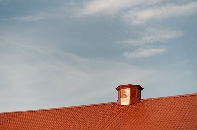 Red tiled roof with a small, wooden cupola under a clear blue sky. The scene conveys a sense of calm and simplicity.