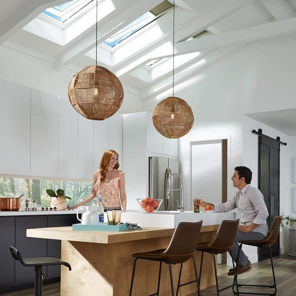 Modern kitchen with skylights and pendant lighting. A woman and man sit at a wooden island. Warm tones, relaxed atmosphere, and sleek decor.