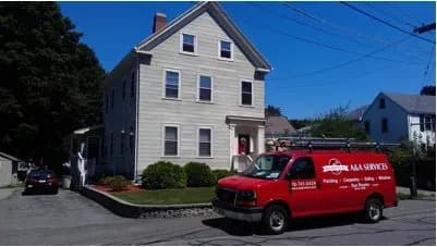 A red service van labeled "AAA Services" is parked on the street beside a beige, three-story residential house under clear blue skies.