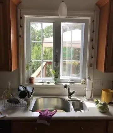 Bright kitchen scene with a window view of greenery, a stainless steel sink, and plants on the sill. Dishes dry on the counter, conveying a cozy, homey feel.
