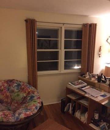 Cozy room with a brown-curtained window, a floral papasan chair, and a cluttered desk filled with papers and books, emitting a warm, homey ambiance.