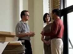 Three people stand in a bright room, engaged in conversation. The setting suggests a professional or collaborative environment, conveying focus and engagement.