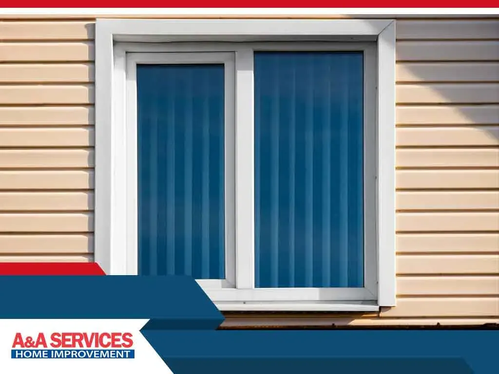 A rectangular window with blue blinds is set in a beige vinyl siding wall. The scene is framed with the A&A Services Home Improvement logo at the bottom left.