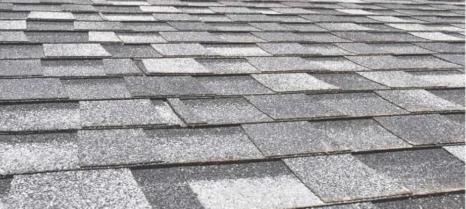 Gray asphalt roof shingles laid in an overlapping pattern, with varying shades creating a textured, checkered effect. The image conveys durability and uniformity.