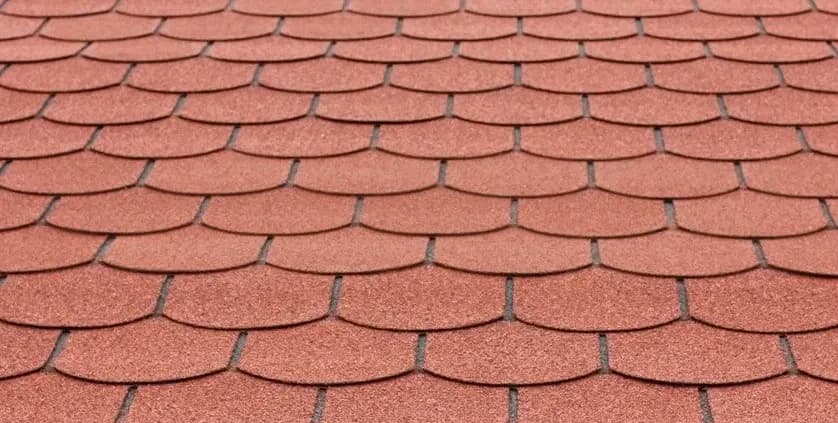 Red roof shingles arranged in a neat, overlapping pattern, creating a uniform, textured surface. The image conveys a sense of structure and durability.
