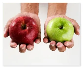 Two hands holding apples; the left hand holds a red apple, the right a green one. The white background emphasizes the contrast between the fruits.