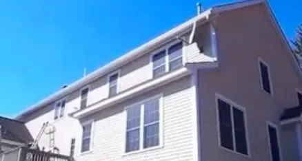 Two-story beige house with a sloped roof, white trim, and multiple large windows, set against a clear blue sky, creating a calm and inviting atmosphere.