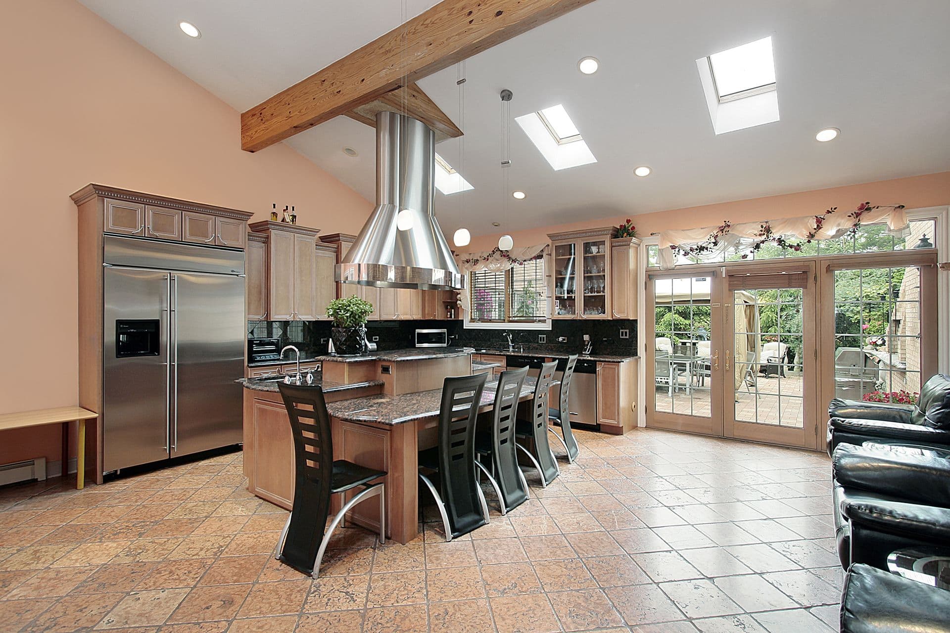 Spacious kitchen with high ceilings, skylights, and large windows. Modern island with bar stools, stainless steel appliances, and tile floor. Bright and inviting.