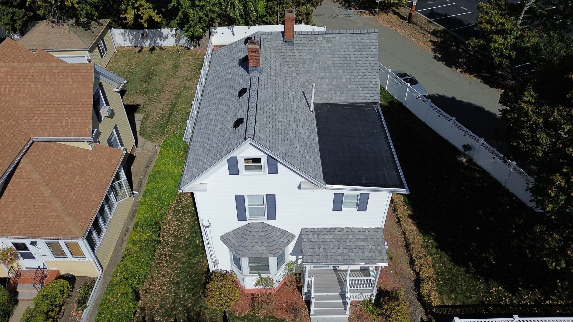 Aerial view of a white house with a gray roof in a suburban neighborhood. It features a small front porch and a tidy yard with hedges.