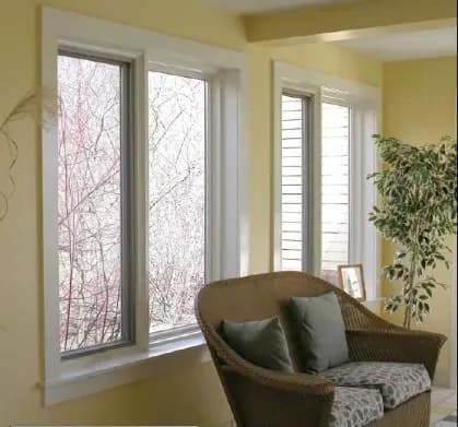 Cozy room with yellow walls features large windows, a wicker chair with green cushions, a leafy plant, and soft natural light creating a serene atmosphere.