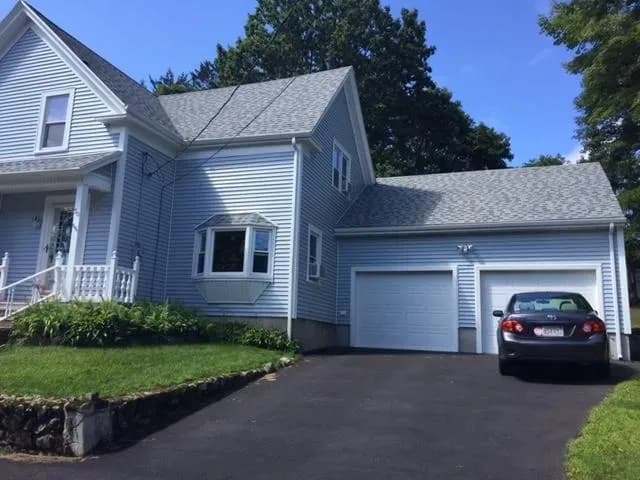 A light blue two-story house with a gabled roof and a neatly trimmed lawn. A black car is parked in the driveway beside the attached garage.
