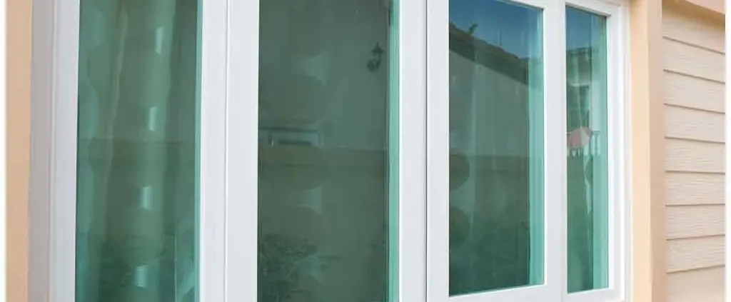 Alt text: "A large white-framed window with four glass panes reflecting the exterior surroundings. The window is set in a beige wall with horizontal paneling."