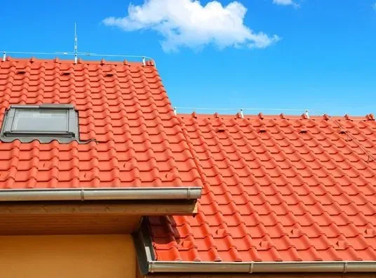 Red tiled roof with a skylight set against a bright blue sky with a few clouds. The vibrant colors suggest a clear and sunny day.