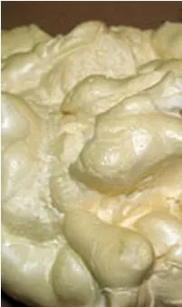 Close-up of beige, foamy textured surface resembling expanding foam. The surface appears puffy and soft, with irregular shapes and glossy highlights.
