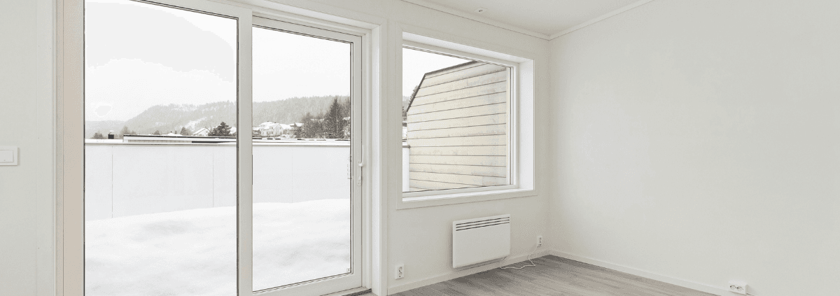 Minimalist bright room with large glass doors and a window overlooking a snowy landscape. Light wood floors and neutral walls create a serene atmosphere.