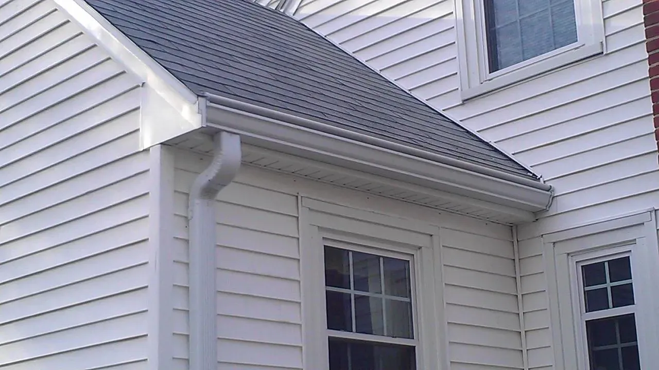White siding house corner with two windows, a gray shingled roof, and a rain gutter. The clean lines and bright tones convey a well-maintained exterior.