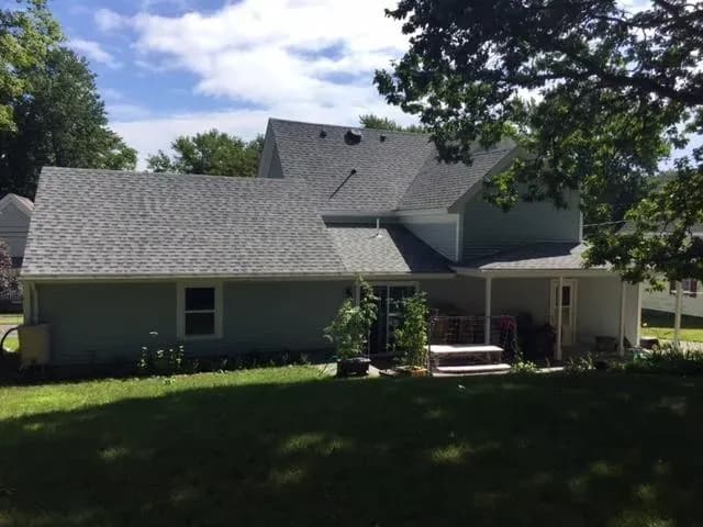 A suburban home with gray siding and a gabled roof under a bright sky. The backyard features a small garden and a wooden bench, creating a peaceful atmosphere.