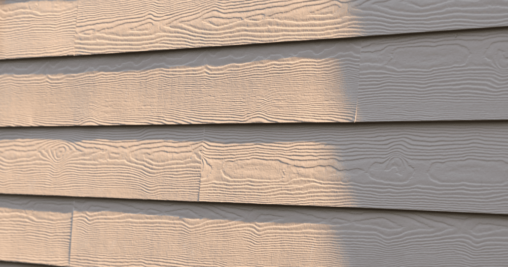 Close-up of beige wood-textured siding with horizontal lines, partially lit by sunlight creating soft shadows. The pattern mimics natural wood grain.