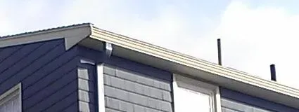 The image shows the slanted roof of a blue building with horizontal siding and two small chimney pipes. The sky is partly cloudy in the background.