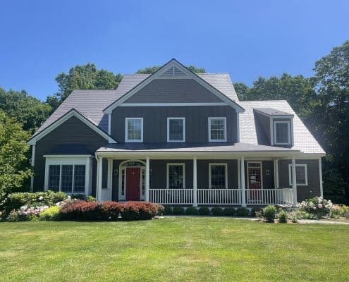 A charming two-story house with navy blue siding, white trim, red doors, and a welcoming porch, surrounded by a lush green lawn and bushes.