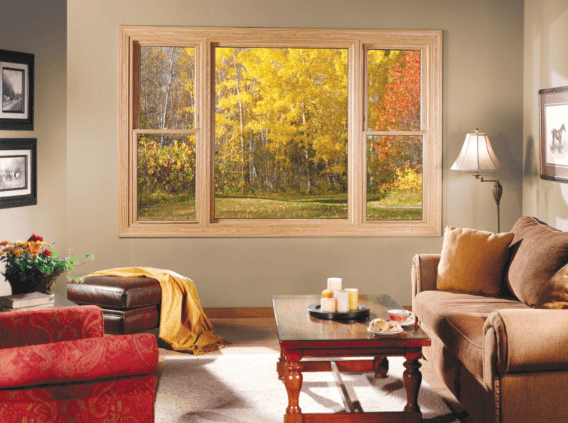 Cozy living room with autumn view through a large window. Brown sofa, red armchair, and warm lighting create an inviting, serene atmosphere.