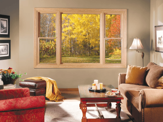 Cozy living room with a large window showing vibrant autumn trees. Warm tones, a soft brown sofa, red armchair, and a wooden coffee table create a welcoming atmosphere.
