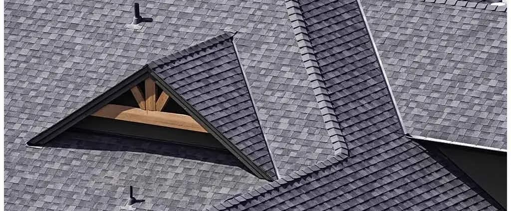 A series of intersecting gray shingled rooftops with visible wooden beams beneath a triangular gable. The design is geometric and orderly.