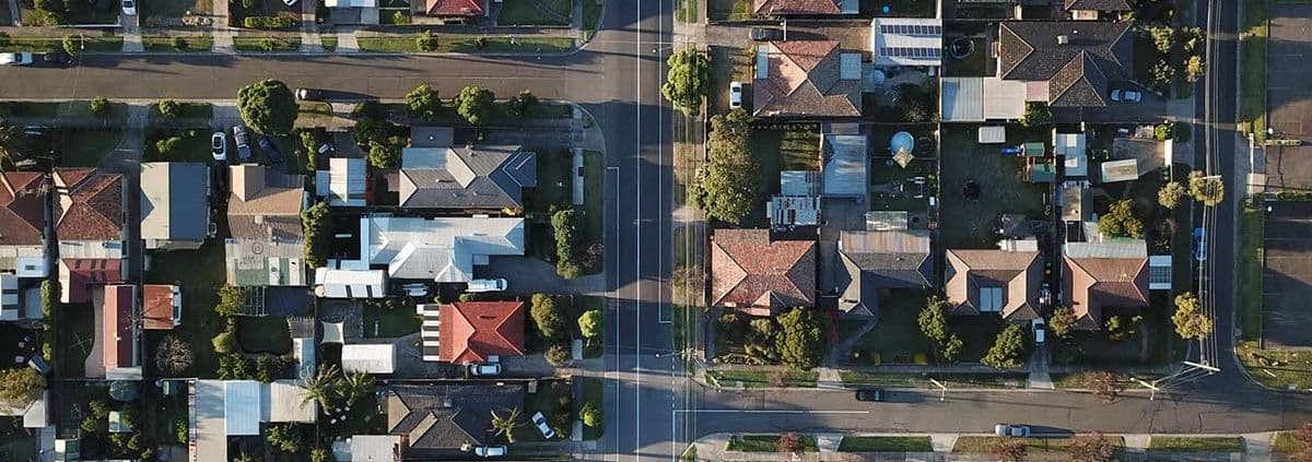 Aerial view of a suburban neighborhood with neatly aligned houses, green lawns, and tree-lined streets, conveying a sense of community and order.